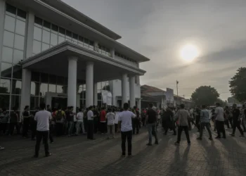 Sebuah adegan protes di luar Mapolsek Makassar dengan warga yang berkumpul di depan pintu masuk. Bangunan polisi modern dengan dinding putih dan jendela besar yang menangkap cahaya sore. Pintu masuk d