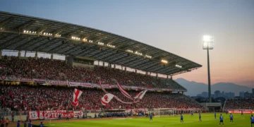 Gelora Bung Karno Stadium is filled with enthusiastic Persib fans in red and white, preparing for a match against Madura United. The modern stadium structure with its curved roof and the bustling crow