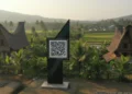 iOS 17.3 untuk iPhone Segera Rilis Desa Sumber Pasir is depicted with a QR code signboard at the entrance, integrating modern technology with traditional rural architecture. The scene showcases a harmonious blend of old and new, symbol