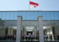 The main building of PDI-P is shown with its red and white flag, modern glass facade, and grand entrance. The interior is bright and spacious, with officials and supporters inside. The building is set