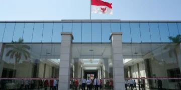 The main building of PDI-P is shown with its red and white flag, modern glass facade, and grand entrance. The interior is bright and spacious, with officials and supporters inside. The building is set