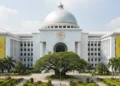 A grand legislative building in South Sulawesi, symbolizing the Golkar Party. The building features a prominent dome, a golden shield emblem, and a well-maintained green landscape, representing the pa