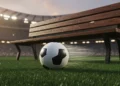 Bola sepak profesional bersandar pada rumput hijau stadion yang basah dengan pencahayaan dramatis malam hari dan latar belakang lampu tribun yang kabur; tidak ada pemain atau logo terlihat.