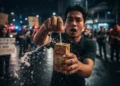 Close-up photograph showing a person receiving a box of Teh Botol Sosro tea that leaks white soap-like fluid when opened, captured against a backdrop of nighttime protests in Jakarta.