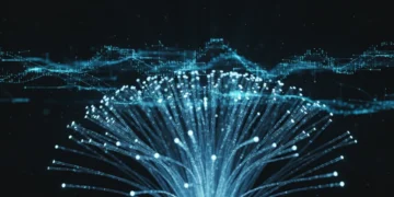 Foto makro kabel serat optik bersinar yang saling bertaut dengan aliran data transparan berbentuk hologram melayang di atasnya terhadap latar belakang hitam pekat. Cahaya biru volumenya menerangi pola