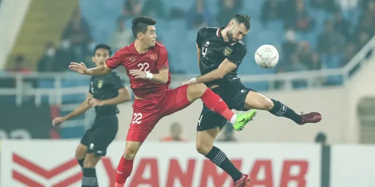 Jersey Emas Champions Edition Timnas Indonesia Resmi Diluncurkan Mitra Teknikal Jersey emas dengan hiasan benang bordir detail bertekstur diletakkan di atas meja kayu berkilau, diterangi lampu sorot stadion dramatis pada malam hari.