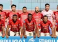 Bola sepak profesional bersandar pada rumput basah bawah sorot lampu stadion dramatis malam hari dengan fokus tajam tekstur detail menunjukkan tetesan air yang memantulkan cahaya sekitar tas peralatan