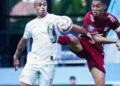 Suasana pertandingan sepak bola malam hari dengan papan strategi taktik kayu bercahaya di bawah sorot lampu stadion yang dramatis dan latar belakang buram dari lapangan rumput basah.